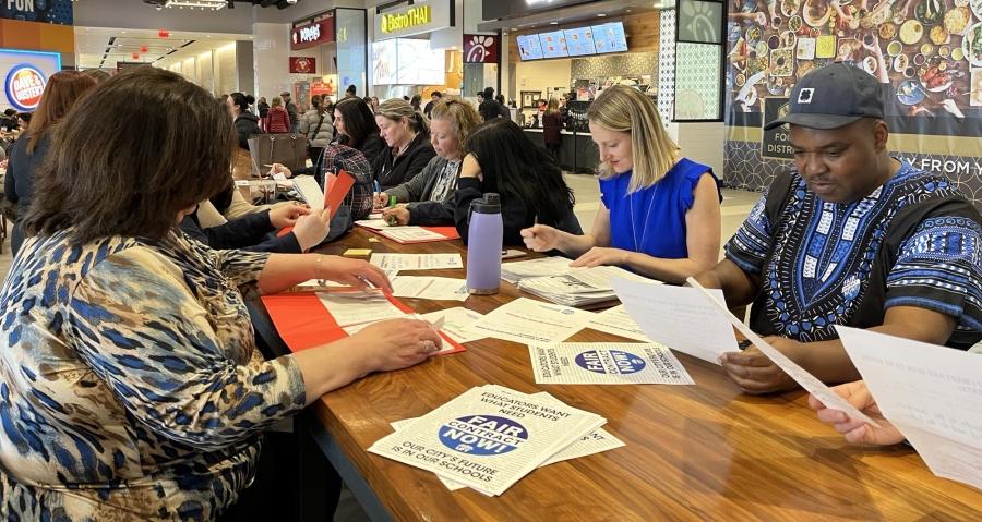 A group of people sit at a food court in a mall completing required paperwork as part of a protest