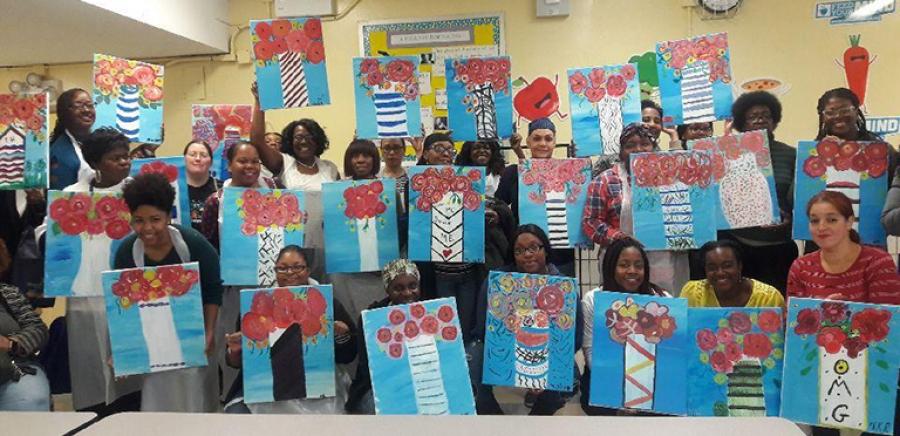 A group of people smiles and holds up paintings of flowers.