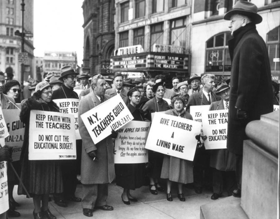 A black and white photo of a man standing on the plinth of a statue speaking to a group of people holding placards with pro-union messaging.