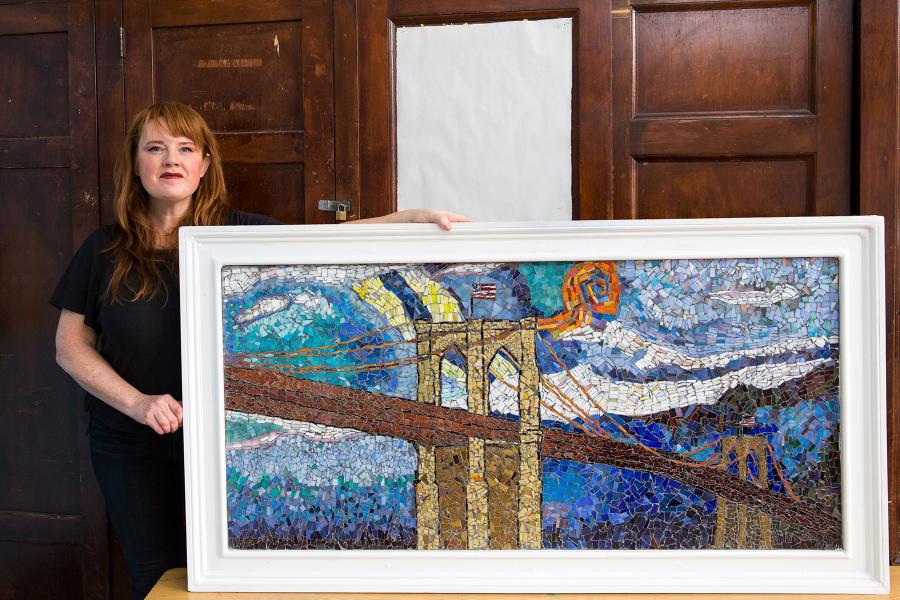 Art teacher Erin McCarthy stands next to the mosaic she created with the help of P369K staff and students in memory of paraprofessional Rulx Dagus.