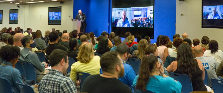 A crowd listens to a man at the podium
