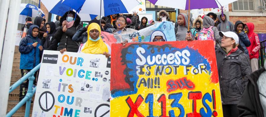 A group of people standing on school steps holding signs