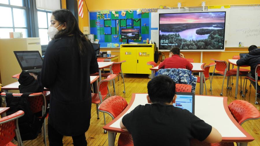 Image of students and teacher in a classroom. The teacher is wearing a mask