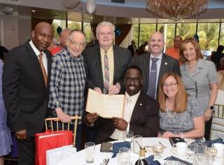 Man seated displays book while others pose for the camera with him