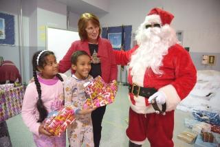 Teacher Diana Wassen looks on as Santa brings smiles to the faces of two PS 65 s