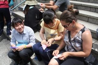 Nagasaki students show Amber Malone (right) how to fold a paper crane at the Ato