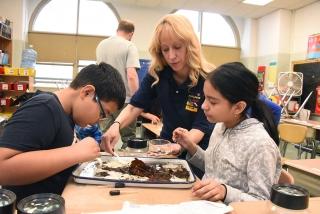 Science teacher Margaret Benitez helps two 5th-graders retrieve tiny creatures l