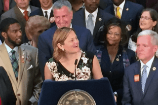 Speaker Melissa Mark-Viverito (at podium) and Mayor Bill de Blasio (behind podiu