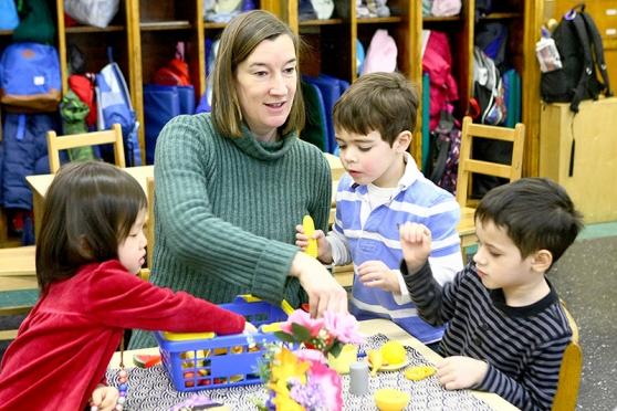 Literacy teacher Noelle O’Reilly helps three 4-year-olds set the table for dinne