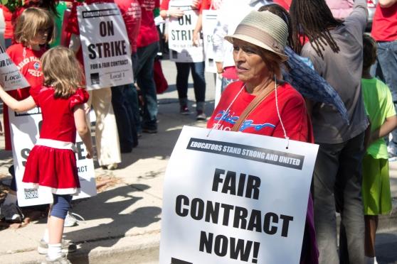Woman wearing red with sign, "Fair contract now"