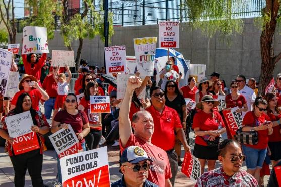 Marchers wearing red and holding signs "Fund our schools now."