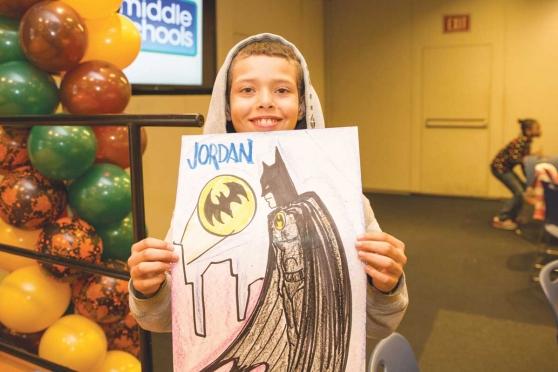 A student proudly shows off the Batman drawing created for him by volunteer Jose