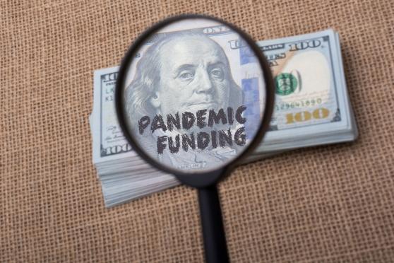 Clipart image of a magnifying glass showing the words "pandemic funding" on a dollar bill