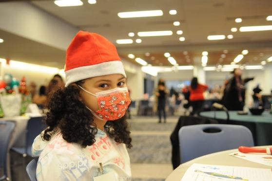 A girl wearing a Santa hat and mask looks at the camera 