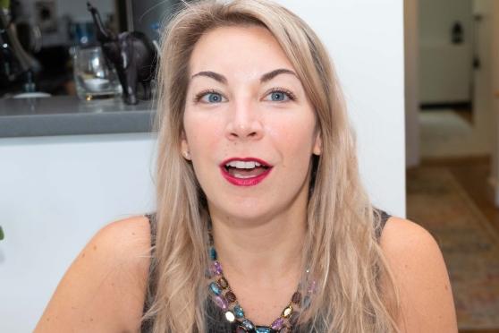 A teacher smiles at her workspace with her kitchen in the background