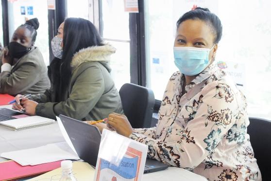 A woman wearing a mask sitting at an information desk smiles under the mask for a photo 