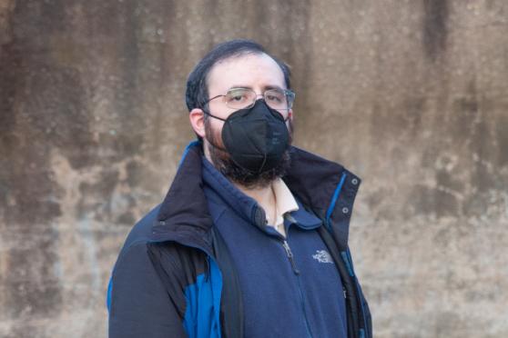 Samuel Berck takes a photo at a public schoolyard. He is standing and wearing a black N95 mask