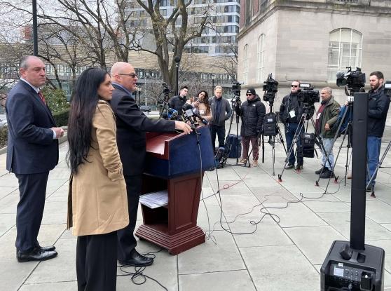 Two men and a woman stand at the podium addressing the congestion pricing lawsuit against the city. 