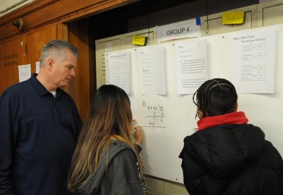 A teacher helps students at a white board. 