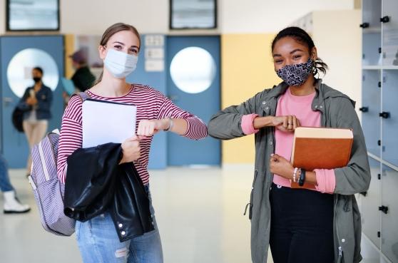 Two teachers wearing masks bump elbows instead of shaking hands. 