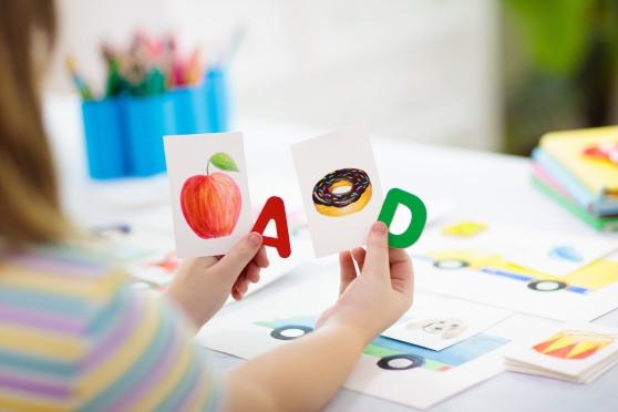 A child holding letters A and D with pictures of an apple and a doughnut 