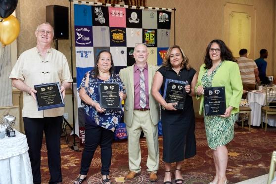 Five people pose for a photo with the two on each end holding awards. 