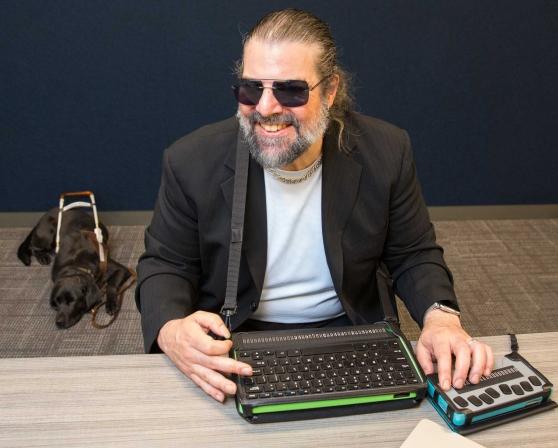 A blind man works on a custom computer with his dog behind him napping