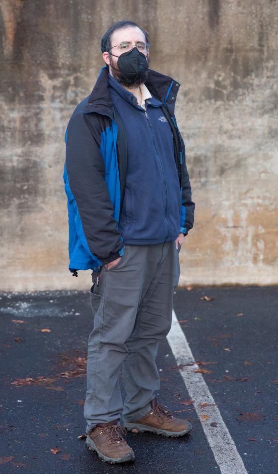 Samuel Berck takes a photo at a public schoolyard. He is standing and wearing a black N95 mask