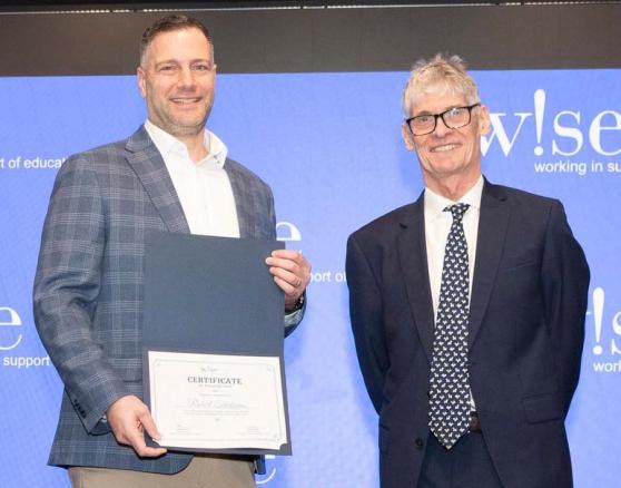 Award-winning teacher Robert Trialonas is congratulated by David Anderson, president and CEO of W!se.