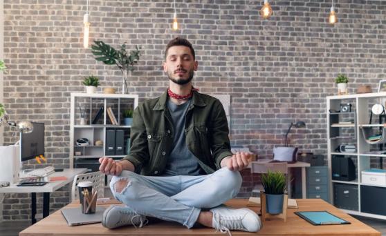 Man meditating while sitting on top of his desk at work
