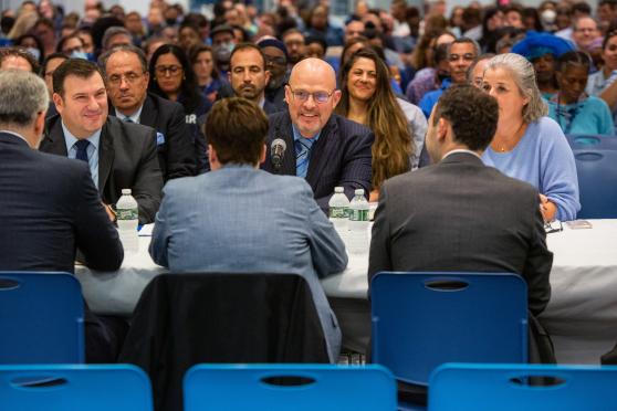 A crowd looks on as two sides discuss at a negotiating table