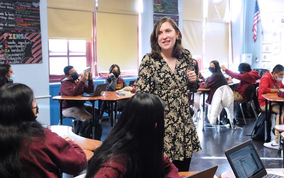 Female teacher standing in room with others who are sitting.