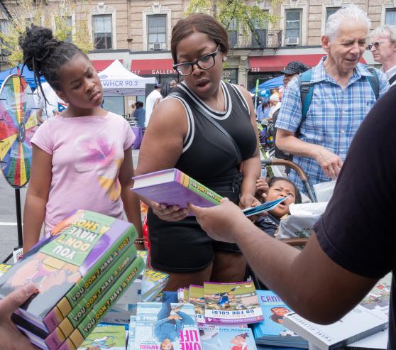 Families explore the selection of books available for the taking, as well as backpack and parent resources, at the UFT's Harlem Week booth. 