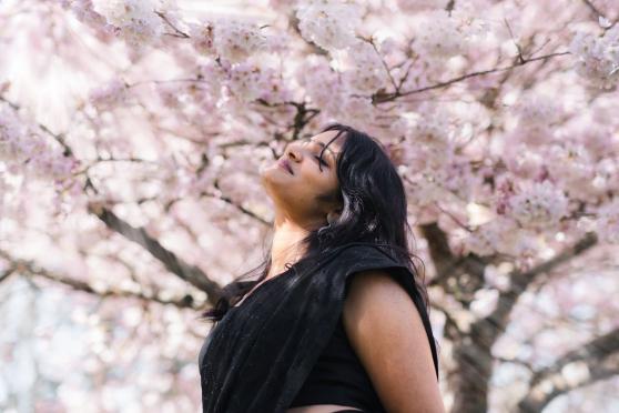 Woman standing in front of a cherry blossom tree looking peaceful.