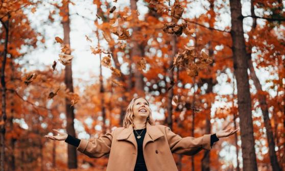 woman-smiling-with-arms-open-as-leaves-fall-in-autumn-forest