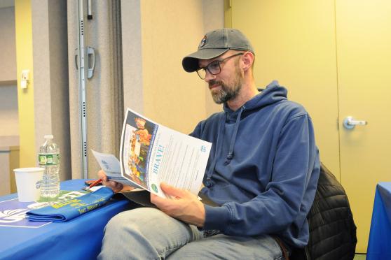 A man sits at a table and reads a pamphlet 