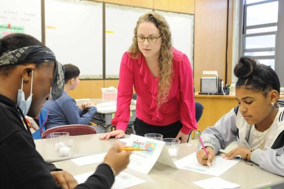 Teacher standing over students working at a desk