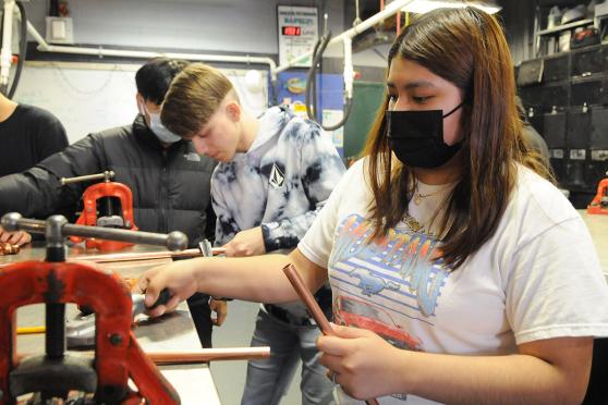 Masked female student holding pipe in hand, male students in the background