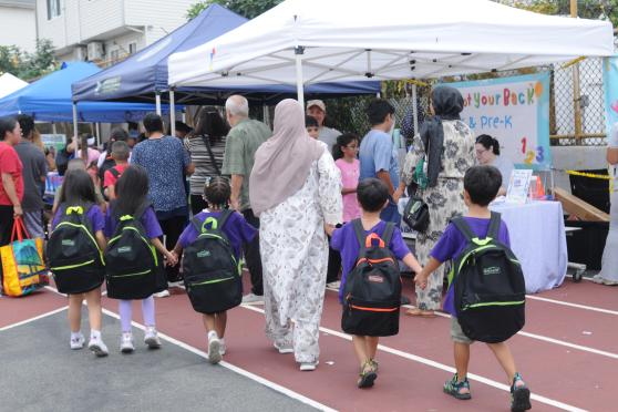 Young students — all holding hands and wearing matching shirts and their new backpacks — are guided through the 5th annual UFT Staten Island Back-to-School Barbecue. 