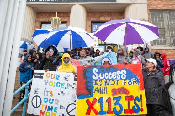 A group of people standing on school steps holding signs
