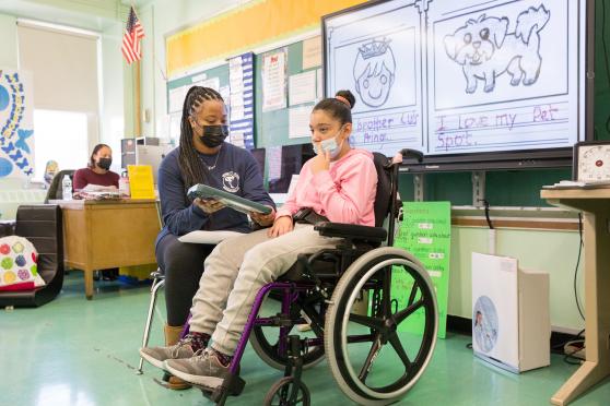 Paraprofessional Dana Capron taps out a young author’s book on an assistive device. 