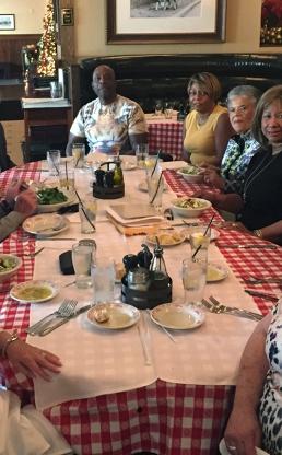 Women and men sitting at a table with a red checkered tablecloth
