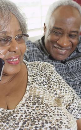 Elderly man and woman sitting next to each other smiling while woman speaks on the phone
