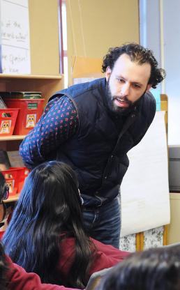 Male teacher stands in classroom with Spanish language written on chalkboard