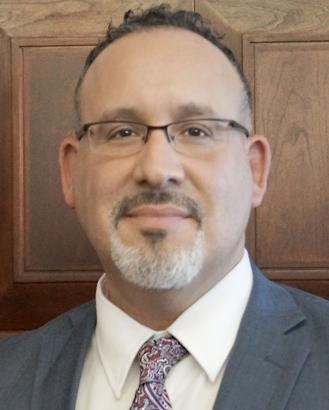 A headshot of Miguel Cardona